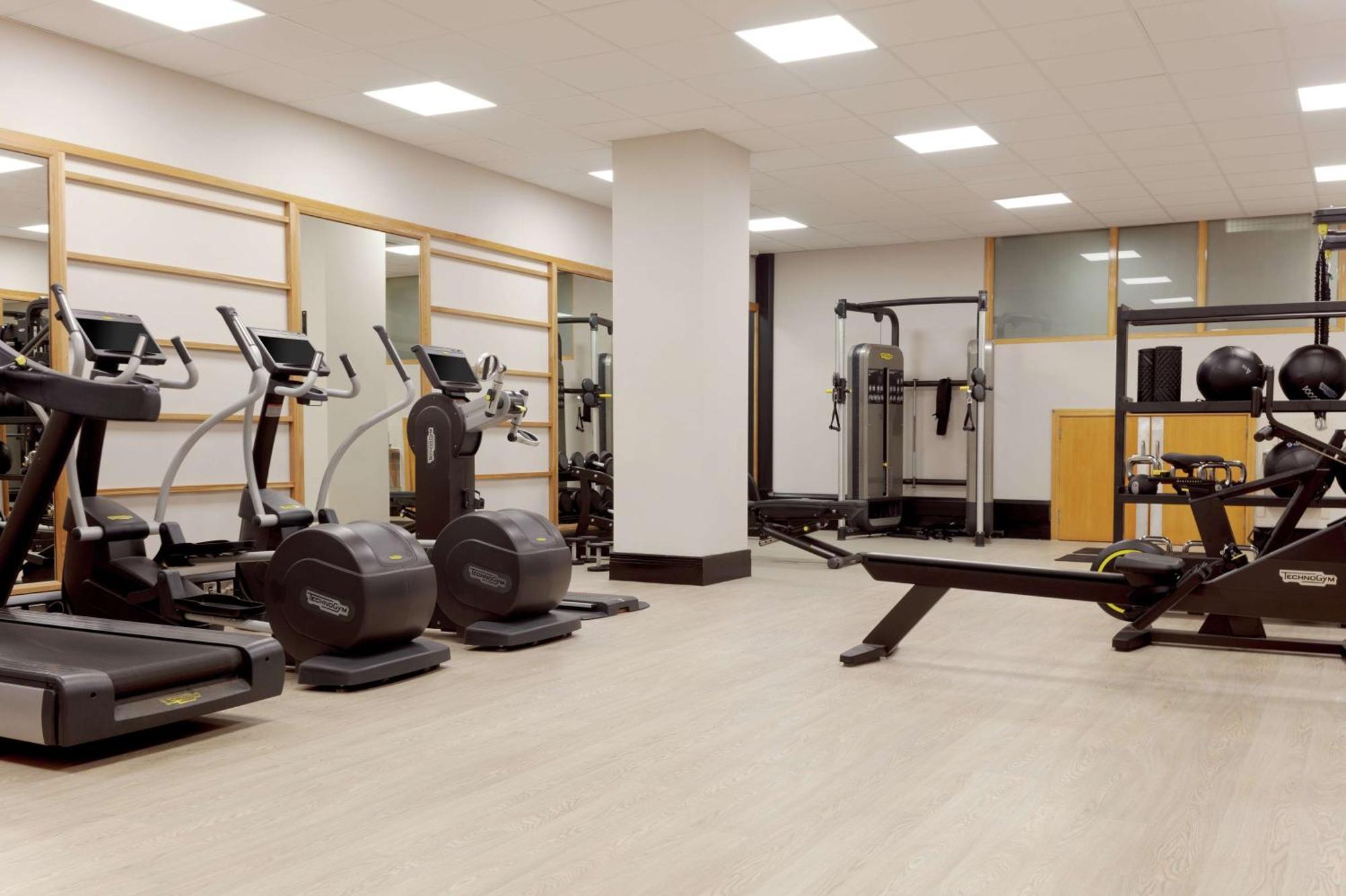 Hilton Belfast Hotel Екстериор снимка The photo shows a gym or fitness area. It features several exercise machines, including treadmills and elliptical machines. There's also a rowing machine and a multi-station strength training equipment. The space is well-lit with overhead lights and 