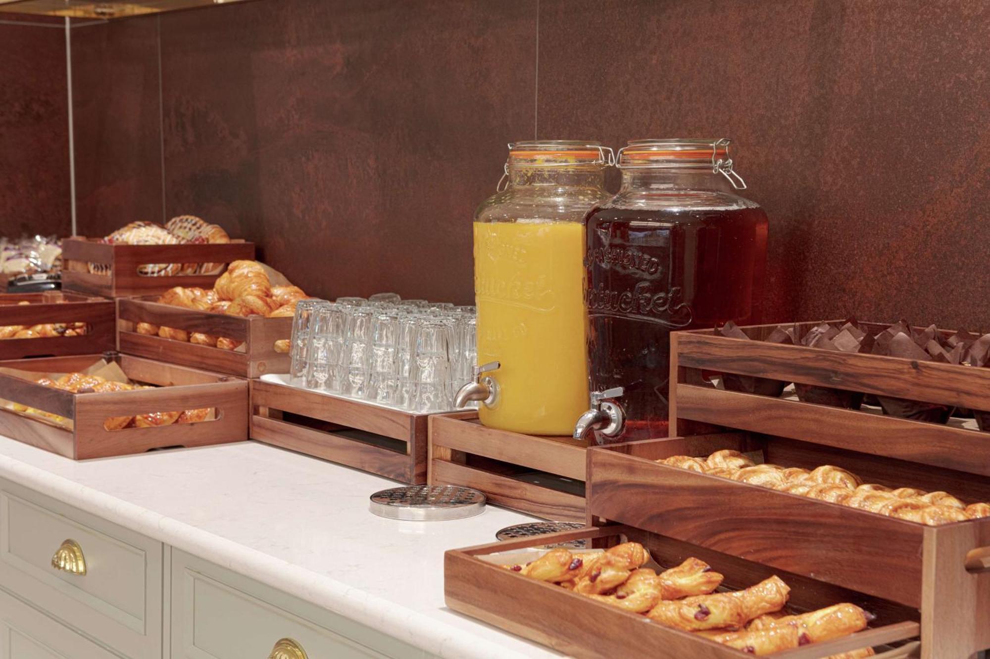 Hilton Belfast Hotel Екстериор снимка The photo shows a buffet-style setup featuring various food and beverage items. There are several wooden trays filled with pastries, including croissants and other baked goods. In the background, there are two large glass jars, one filled with yellow